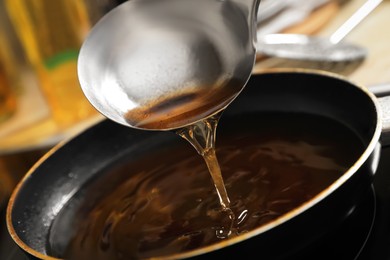 Pouring used cooking oil with ladle onto frying pan on stove, closeup