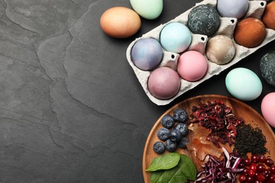 Photo of Naturally painted Easter eggs on black table, flat lay. Red cabbage, spinach, hibiscus, tea, onion, cranberries and blueberries used for coloring