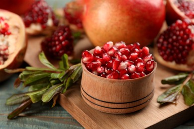 Delicious ripe pomegranate kernels in bowl on wooden board, closeup