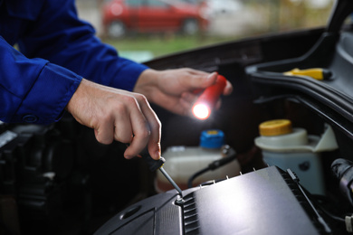 Photo of Mechanic with flashlight fixing car outdoors, closeup