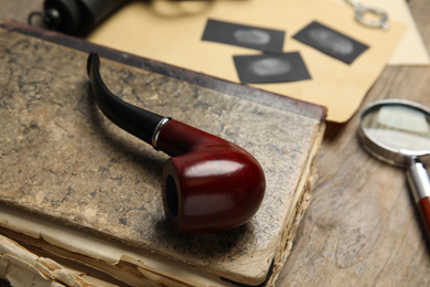 Tobacco pipe and old book on wooden table, closeup. Detective's workplace