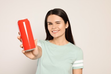 Photo of Beautiful young woman holding red tin can with beverage on light grey background