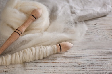 Soft wool and spindles on white wooden table, closeup