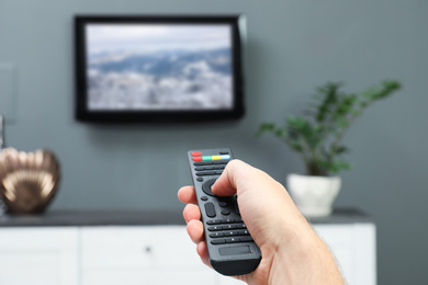 Man switching channels on TV with remote control at home
