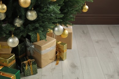Beautifully decorated Christmas tree and many gift boxes near brown wall indoors, closeup. Space for text