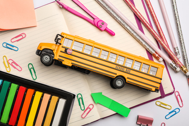 Flat lay composition with yellow school bus model on white background. Transport for students