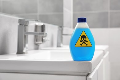 Bottle of toxic household chemical with warning sign in bathroom, space for text
