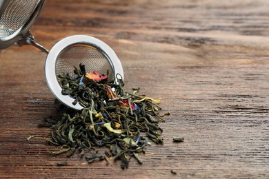 Photo of Snap infuser with dried herbal tea leaves on wooden table, closeup. Space for text
