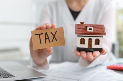 Woman holding house model and card with word TAX, closeup