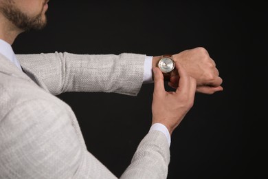 Businessman looking at wristwatch on black background, closeup. Time management