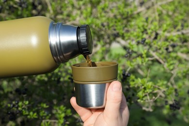 Man pouring hot drink into mug outdoors, closeup