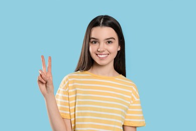 Photo of Teenage girl showing peace sign on light blue background