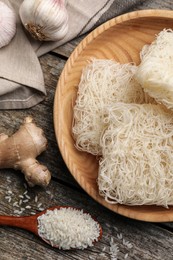 Bowl with dried rice noodles and ingredients on wooden table, flat lay