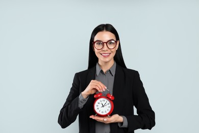 Businesswoman holding alarm clock on light grey  background. Time management