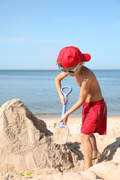 Cute little child playing with plastic shovel at sandy beach on sunny day