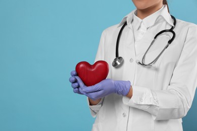 Photo of Closeup view of doctor with stethoscope and red heart on light blue background, space for text. Cardiology concept