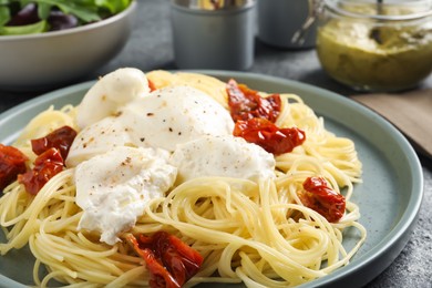 Delicious spaghetti with burrata cheese and sun dried tomatoes on grey table, closeup
