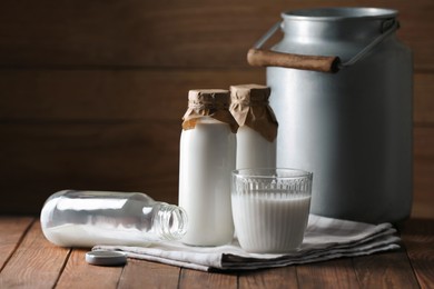 Tasty fresh milk in can, bottles and glass on wooden table, space for text