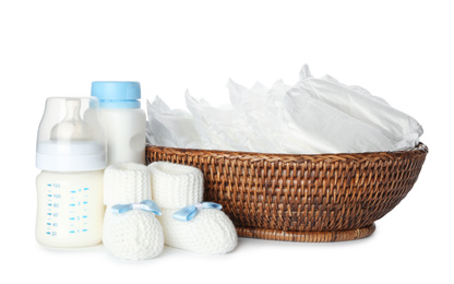 Photo of Wicker bowl with disposable diapers, child's booties and bottles on white background