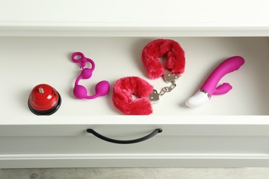Different modern sex toys in open wooden drawer, above view