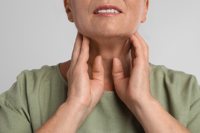 Mature woman doing thyroid self examination on light grey background, closeup