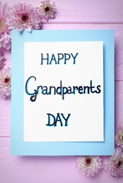 Beautiful flowers and card with phrase Happy Grandparents Day on pink wooden table, flat lay