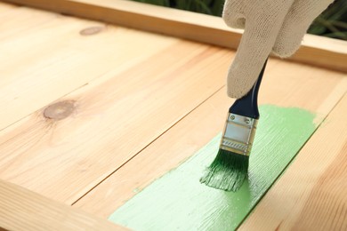 Worker applying green paint onto wooden surface, closeup. Space for text