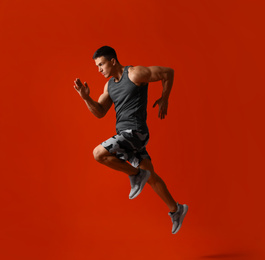 Athletic young man running on red background, side view