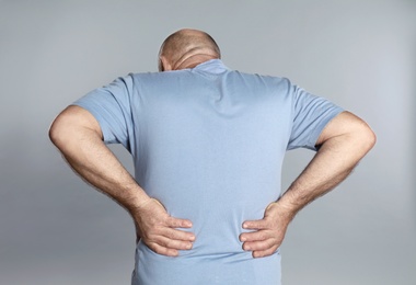 Mature man suffering from backache on light grey background