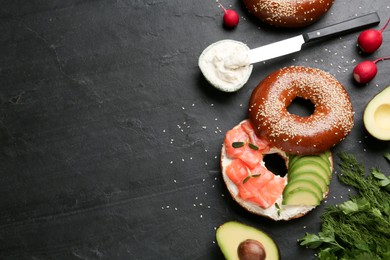 Photo of Delicious bagel with cream cheese, salmon and avocado on black table, flat lay. Space for text
