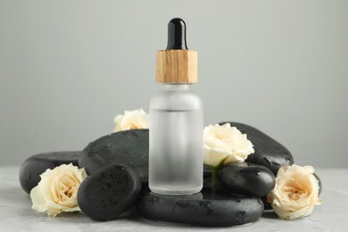 Bottle of face serum with spa stones and beautiful roses on wet table against grey background, closeup