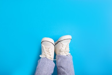 Photo of Little baby in stylish gumshoes on light blue background, top view. Space for text