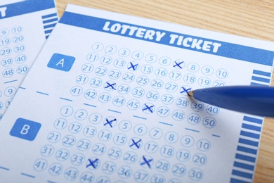 Filling out lottery tickets with pen on wooden table, closeup. Space for text