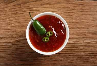 Spicy chili sauce in bowl on wooden table, top view