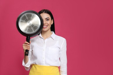Photo of Young housewife with frying pan on pink background, space for text