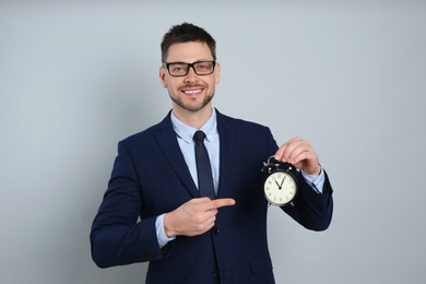 Happy businessman pointing on alarm clock against grey background. Time management
