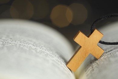 Christian cross on open Bible against blurred background, closeup