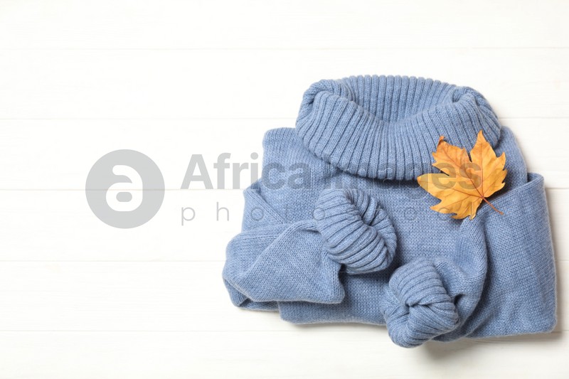 Photo of Top view of warm sweater and dry leaf on white wooden background, space for text. Autumn season