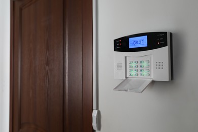 Home security alarm system on white wall near door, space for text