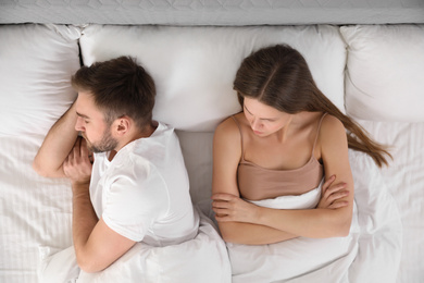 Upset young woman near sleeping husband in bed, top view. Relationship problems