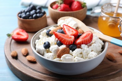 Bowl of fresh cottage cheese, berries and almonds on wooden board, closeup