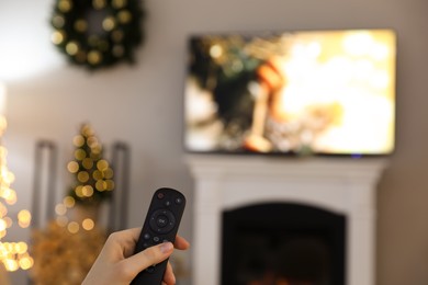 Woman with remote control in room decorated for Christmas, closeup