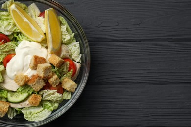 Bowl of delicious salad with Chinese cabbage, tomatoes and bread croutons on black wooden table, top view. Space for text