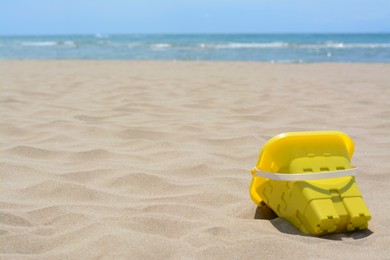Yellow plastic bucket on sand near sea, space for text. Beach toy
