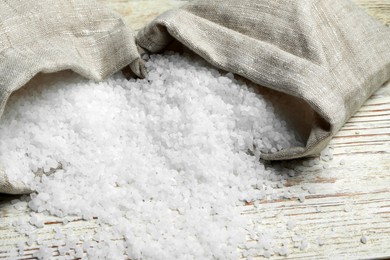 Bags with natural sea salt on white wooden table, closeup