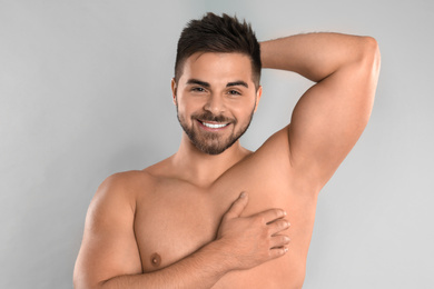 Young man showing hairless armpit after epilation procedure on grey background