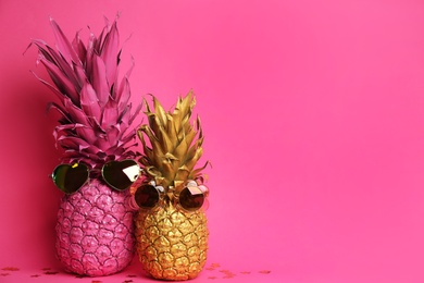 Photo of Painted pineapples with sunglasses on pink background, space for text. Creative concept