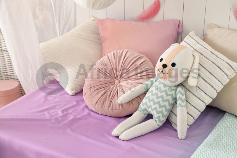 Photo of Comfortable bed with cushions and toy in room. Interior design