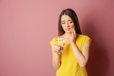 Woman with sensitive teeth holding glass of water on color background