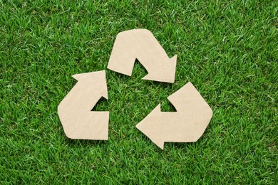 Photo of Cardboard recycling symbol on green grass, flat lay